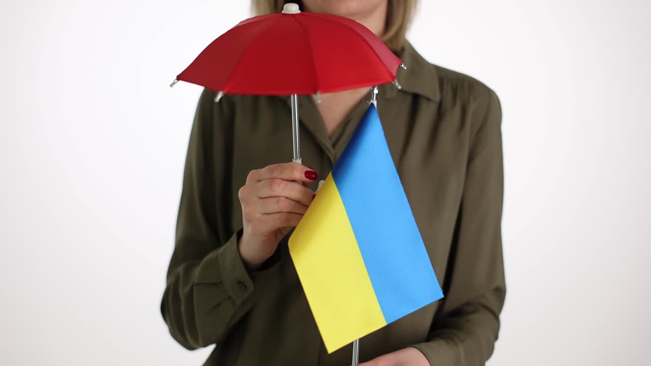 Una donna regge la bandiera nazionale ucraina sotto un ombrello rosso.