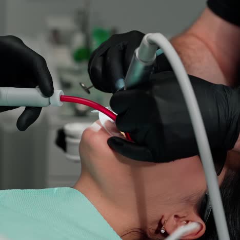 dentist's hands in black gloves treating woman's teeth. stomatologist with assistant use modern methods to treat client's tooth. close-up.