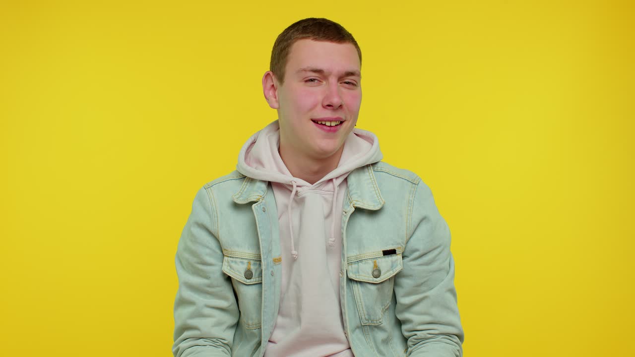 파란색 청바지 재과 분홍색 후디를 입은 젊은 남자가 미소 짓고 카메라에 포즈를 취하고 있습니다.