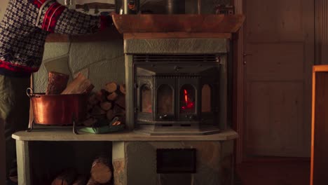 man piling up pieces of cut firewood beside a cast iron wood burning stove fireplace