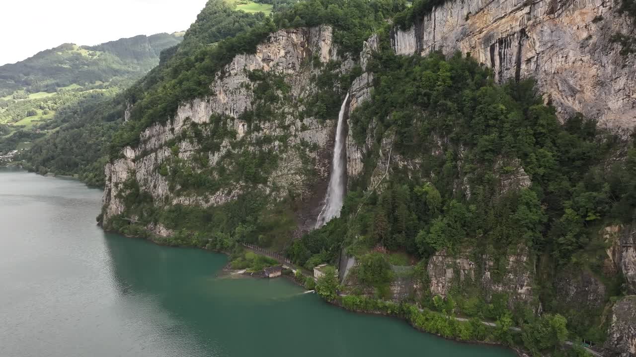 Drone flying backward revealing the stunning Seerenbachfälle waterfall and turquoise Walensee in Switzerland