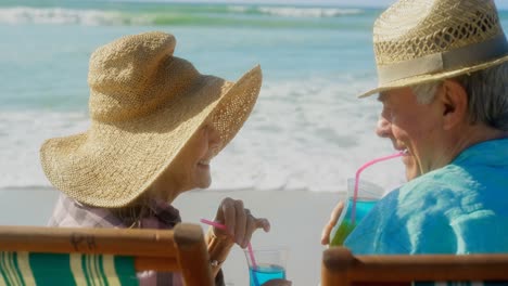 Rückansicht-Eines-Aktiven-älteren-Kaukasischen-Paares,-Das-Am-Strand-Einen-Cocktail-Trinkt,-4k