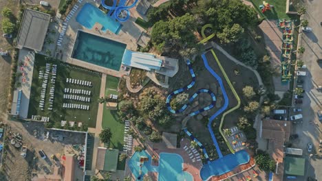 topshot view showcase a vibrant water park filled with sparkling swimming pools, thrilling slides, sun loungers, and lush green trees, creating an inviting summer atmosphere