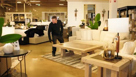 man in black work clothes tests the weight of a coffee table in a furniture store