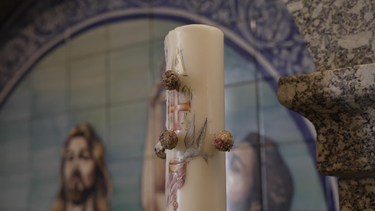 Paschal candle with symbolic decoration placed beside a stone font and blue tile artwork