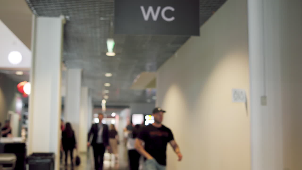 Blurry WC sign in a public hallway with blurred people walking