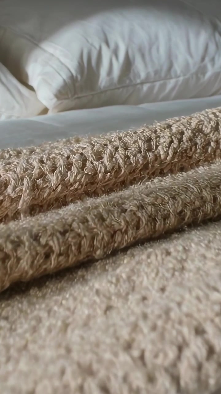 Video verticale: La telecamera si avvicina a un plaid beige in camera da letto, mostrando la trama del filato e un cuscino.