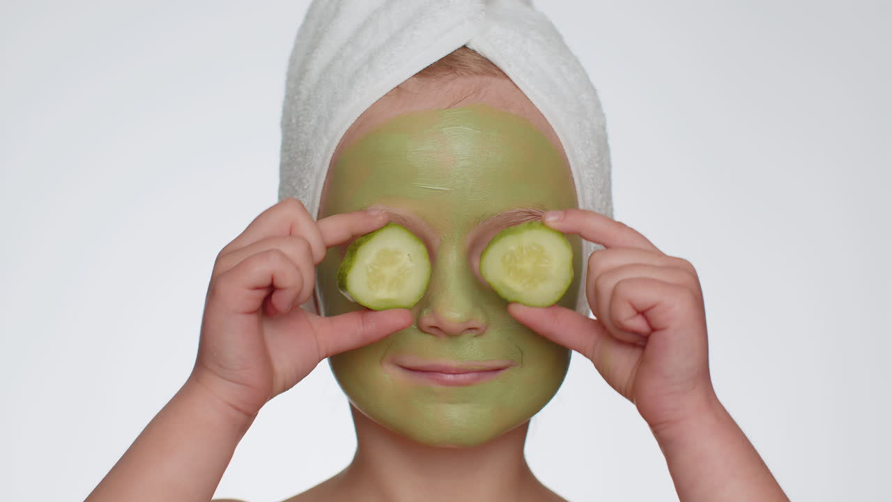 아름다운 미소 어린 소녀 아이 머리에 수건을 착용하고 얼굴에 청소 보습 녹색 마스크를 적용