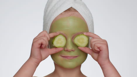 Beautiful-smiling-child-girl-kid-in-towel-on-head-applying-cleansing-moisturizing-green-mask-on-face