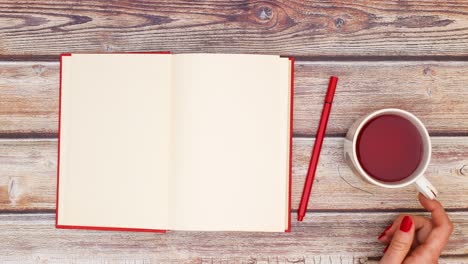 woman hand open red book and put pencil and cup of hot tea on the table - stop motion