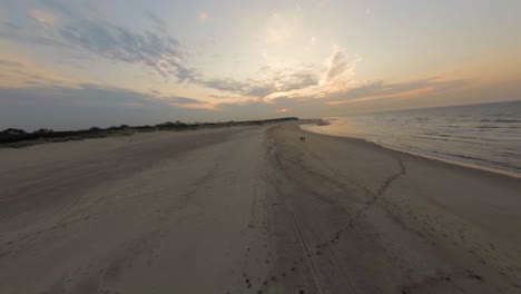 Aerial-drone-flight-above-two-people-walking-on-beach-in-golden-sunset