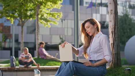 mujer satisfecha terminando el trabajo en el parque de la ciudad de cerca. chica sonriente cerrando los ojos