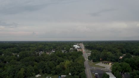 Aerial-drone-forward-moving-over-a-highway-alongside-small-town-houses-set-among-rural-farm-landscape-at-sunset