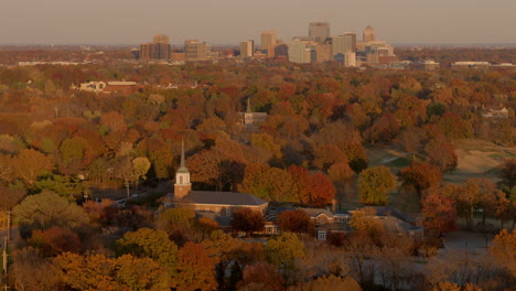 Aerial-of-a-small-church-surrounded-by-trees-with-a-downtown-city-skyline-on-the-horizon