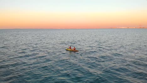 Una-Pareja-Rema-En-Un-Kayak-A-Través-Del-Océano-Del-Medio-Oriente-Durante-Una-Increíble-Puesta-De-Sol,-Antena-De-Drones