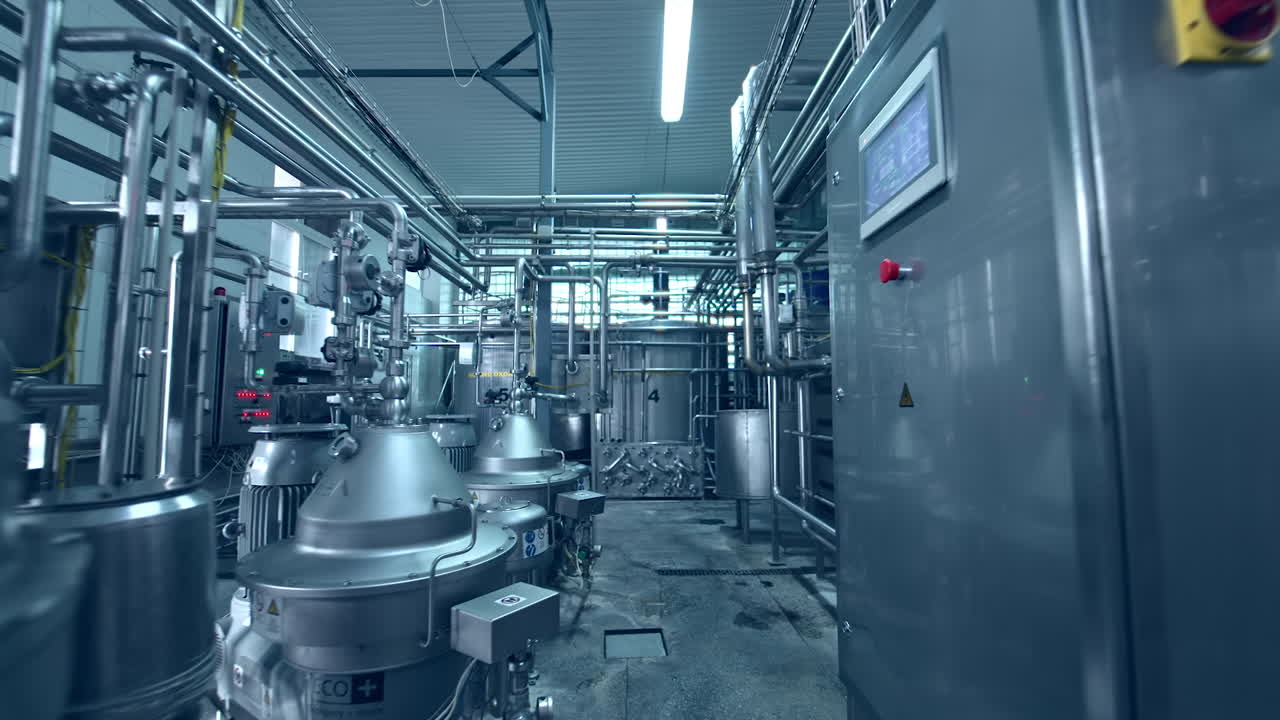 Moving along the impressive and complicated milk factory equipment. Metal pipelines and tanks connected with each other into a system. Dolly shot.