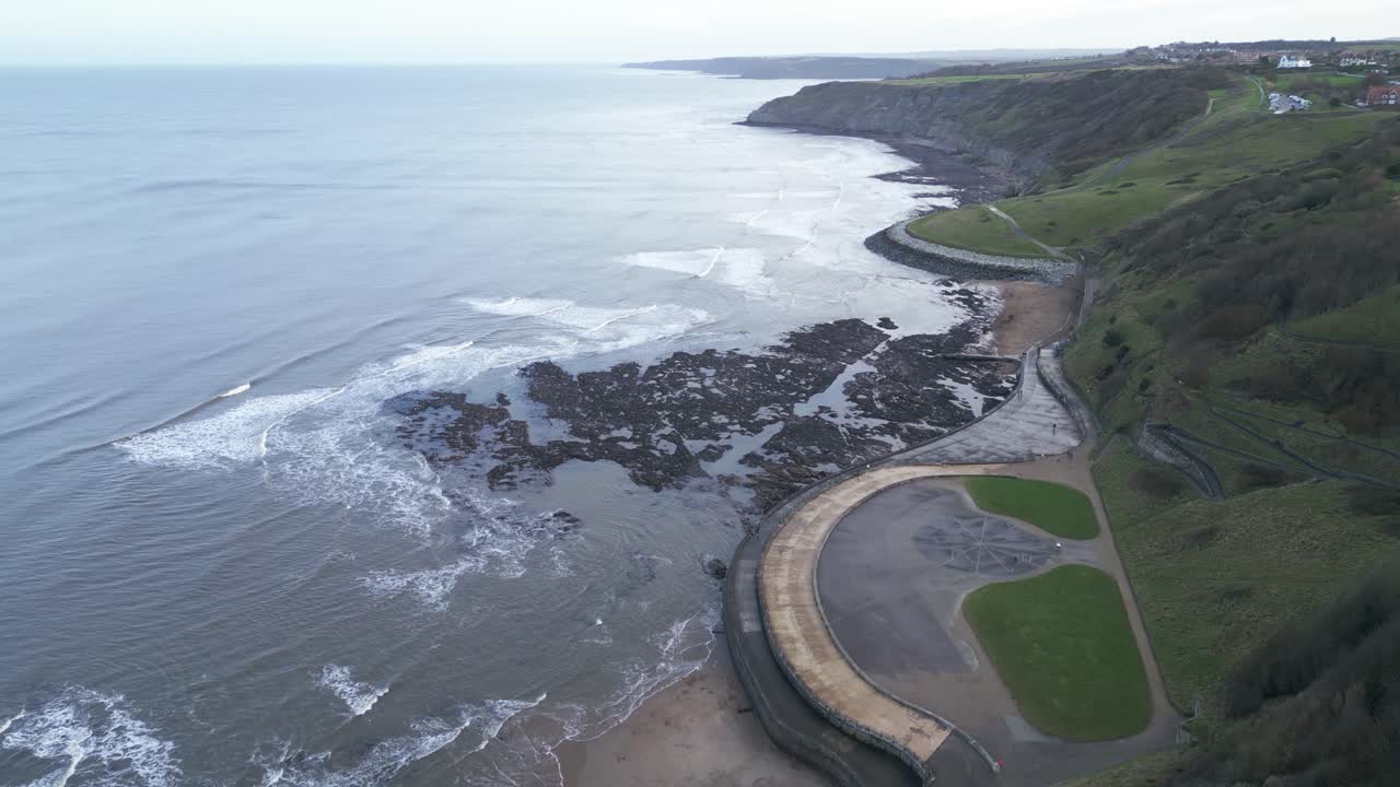 fotografía aérea en cámara lenta de pequeñas olas que se acercan a una tierra vacía y estéril al lado de una colina en la bahía de scarborough, inglaterra