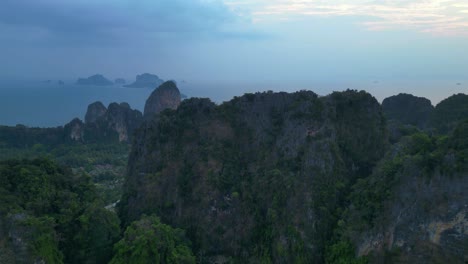 limestone cliffs and lush tropical jungle of railay beach, krabi, thailand, at dusk, creating a dramatic and serene landscape. nice aerial view flight tilt down drone