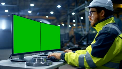 inside the heavy industry factory industrial engineer works on the personal computer with two  green mock-up screens.