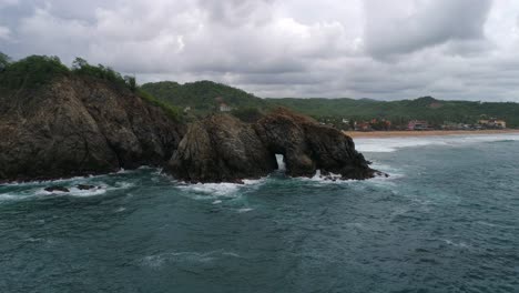 Aerial-shot-of-a-big-rock-formation-with-a-door-in-the-middle,-Zipolite-beach,-Oaxaca