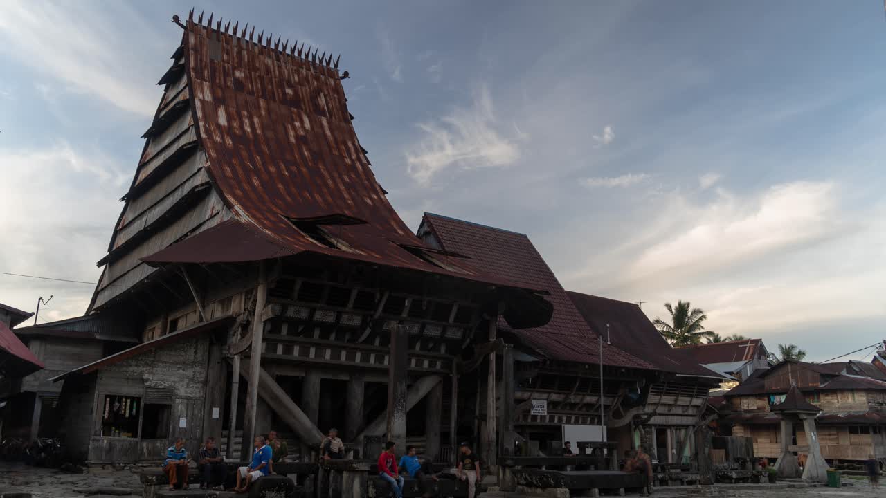 Traditional wooden house with a distinctive peaked roof and people gathered outside