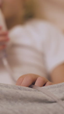 blurry small girl breathes with modern inhaler in comfortable bed in room close focus on kid hand on blanket
