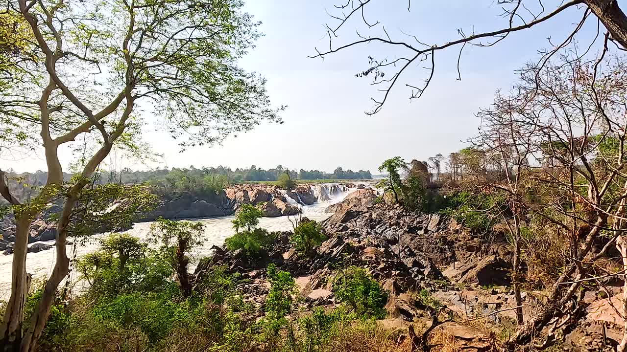 A serene landscape with a waterfall surrounded by lush greenery and rocky terrain under clear skies
