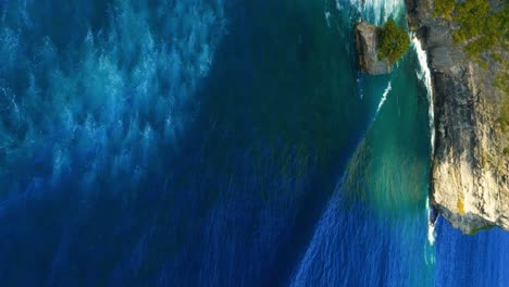 vertical reveal shot of the pura uluwatu temple in bali, with the green cliffs and slow rolling swells in the ocean