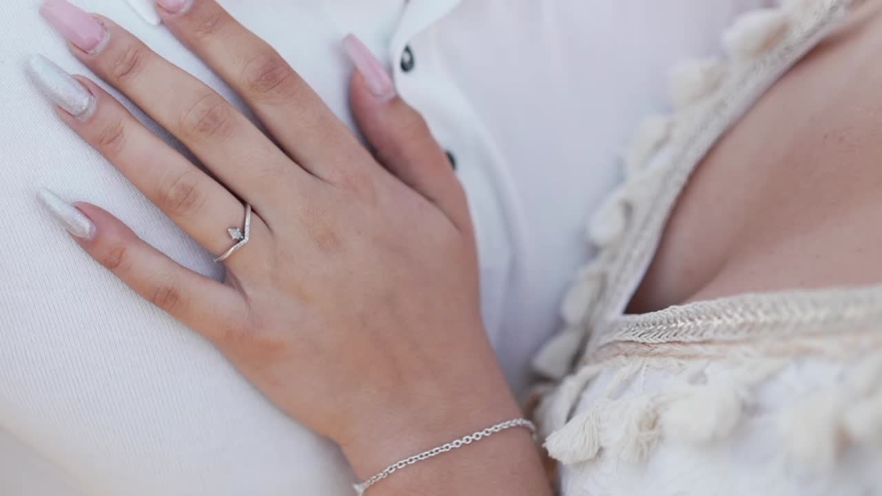 close up of woman's hand with engagement ring resting on man's chest, wearing white shirt