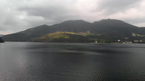 Sideways-flying-aerial-drone-view-out-over-Lake-Ashi-in-Hakone,-Japan-with-mountains-in-distance