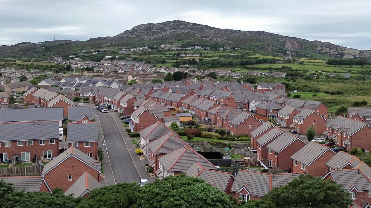 Aerial view circling modern red brick housing neighbourhood under Holyhead mountain in Wales