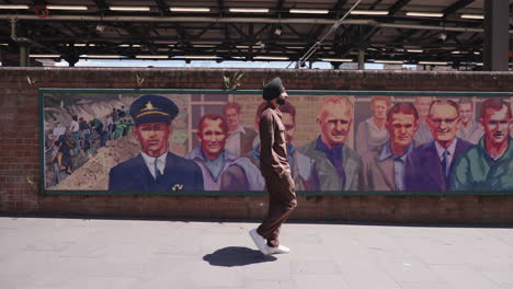 indian punjabi sikh man walking in the street of sydney passing by wall with mural in australia