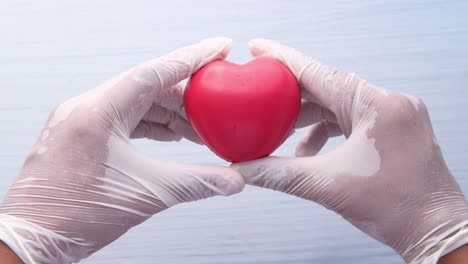 hands in gloves holding a pink heart