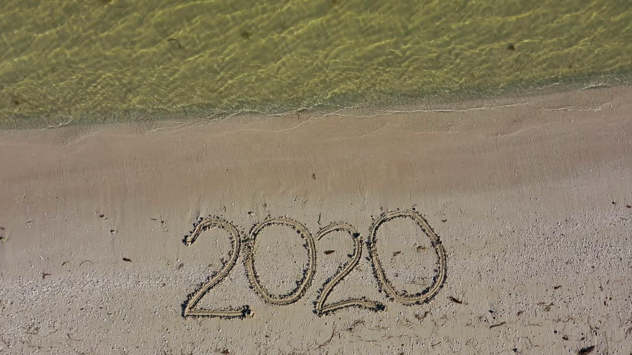 Twenty Twenty written in the sand gets smaller in size as aerial camera moves away