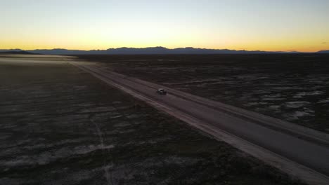 truck driving down a dusty dirt road in a desert basin at sunset - aerial view showing the landscape and mountains in the distance