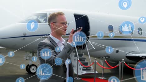 animación de una red de iconos digitales sobre un hombre de negocios caucásico hablando con un teléfono inteligente en el aeropuerto