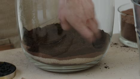 A-young-female-botanist-creates-a-tiny-live-forest-ecosystem-in-a-glass-terrarium---leveling-the-upper-layer-of-soil---a-tight-close-up