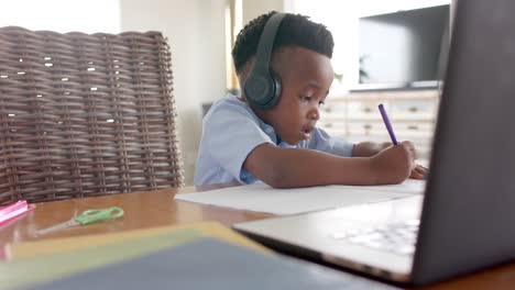 happy african american boy in headphones using laptop for online class at home, slow motion