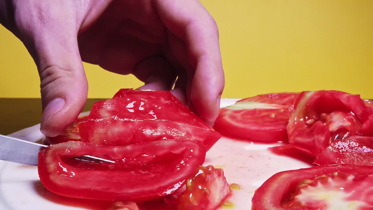 Close-up shot of a man cutting tomato on the desk in slowmotion in front of a yellow background