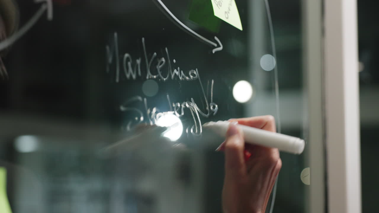 Close Up of Hand Writing Marketing Strategy on Glass Board