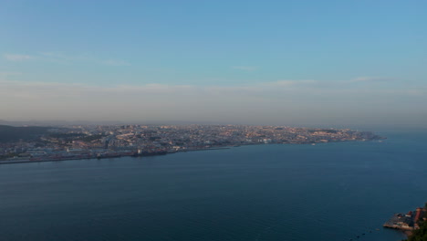 Close-up-back-aerial-view-of-Sanctuary-of-Christ-the-King-statue-on-the-hill-with-reveal-of-urban-city-center-of-Lisbon-on-the-sea-coast