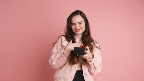 Happy young woman receiving gift box in pink studio
