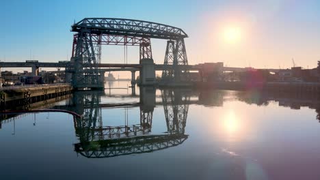 Low-aerial-of-Puente-Transbordador,-still-river-and-low-sun,-Argentina