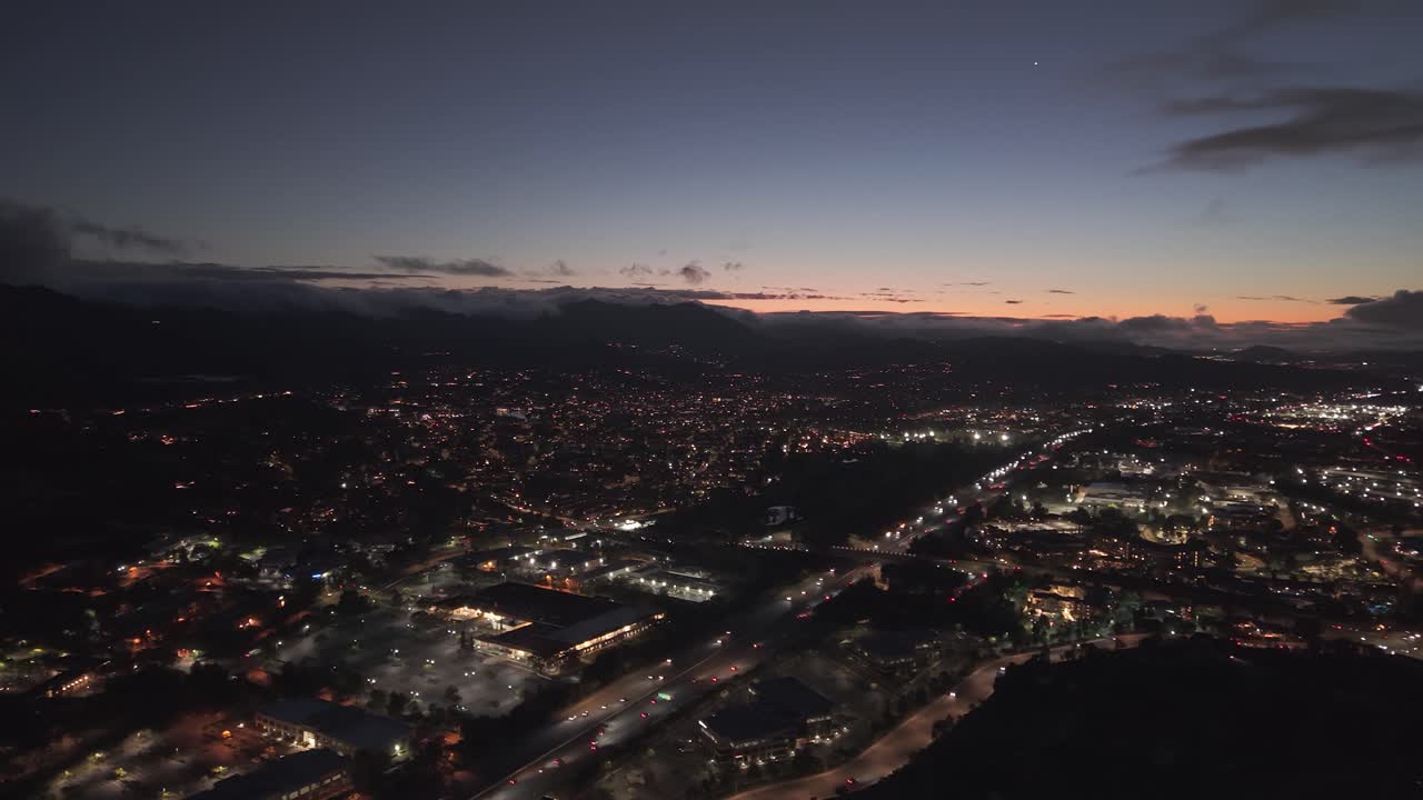 Vista aérea panorámica con dron de Agoura Hills, Los Ángeles, California, EE. UU., al anochecer, con las luces brillantes de la ciudad, el atardecer y las líneas de tráfico que se extienden por el valle en una atmósfera vespertina cinematográfica.