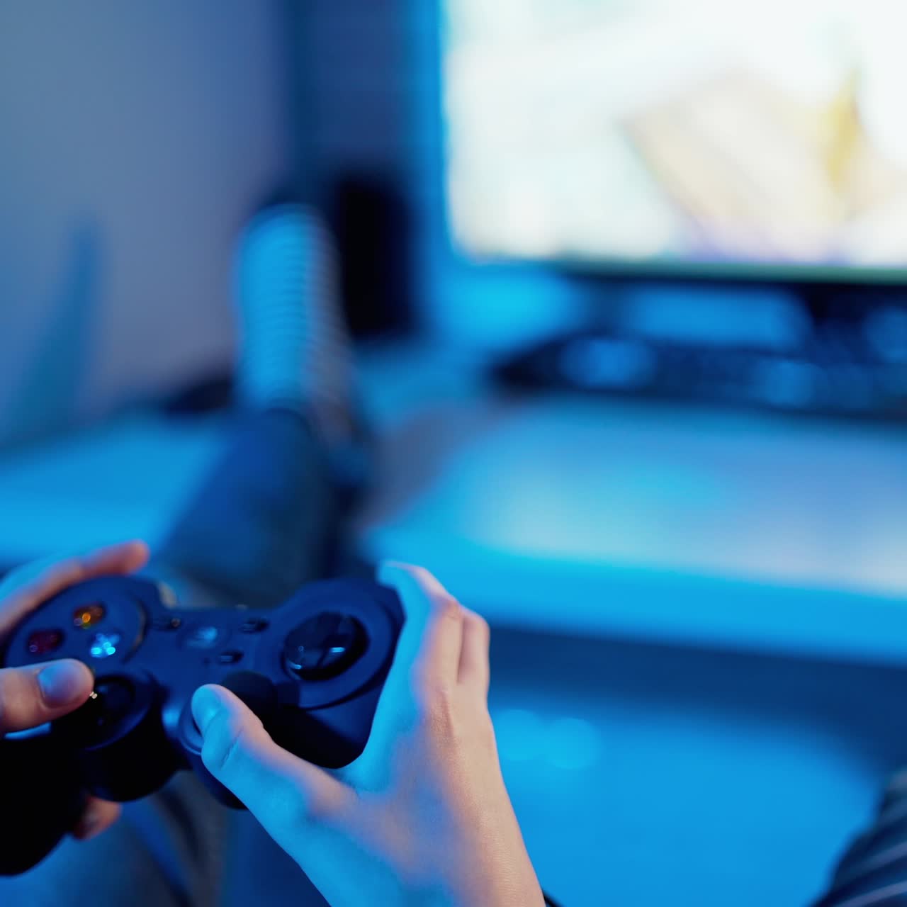 Young gamer playing video game using controller. Joystick in boy's hands in front of the play station screen. Close-up. Blue light.
