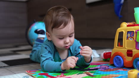 caucasian toddler lies on the floor looking carefully at the black lace. kid turns his head to camera watching it intently. toys around baby.