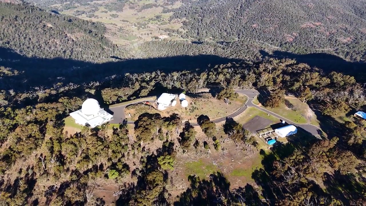 Ripresa aerea con drone dall'alto di cupole di telescopi in cima a una cresta montuosa nel Parco Nazionale di Warrumbungle