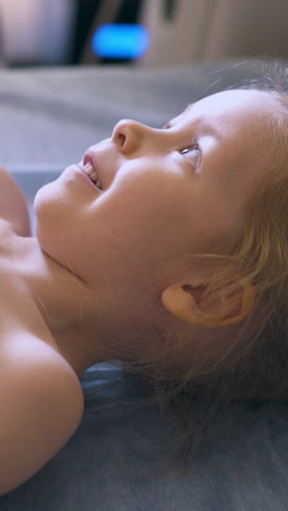 cu: laughing little girl with gel on tummy undergoes abdominal sonogram procedure in light clinic office close view
