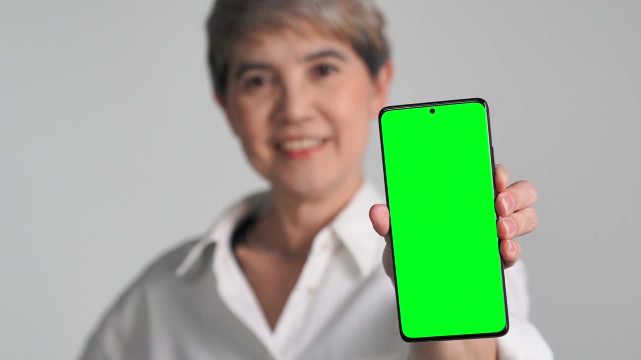 mujer asiática de mediana edad mostrando un teléfono inteligente con pantalla verde