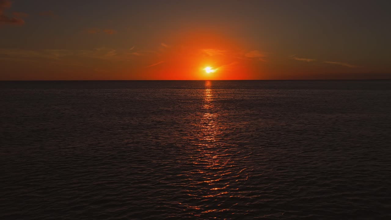The sun sets over the calm caribbean sea with a golden reflection on the water, a serene and romantic scene in Bayahibe. Aerial forward, copy space